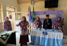 Empat orang pengurus sekolah atau guru sedang berdiri di depan peserta dalam acara formal sekolah, dengan latar belakang spanduk bertuliskan "SD Muhammadiyah".