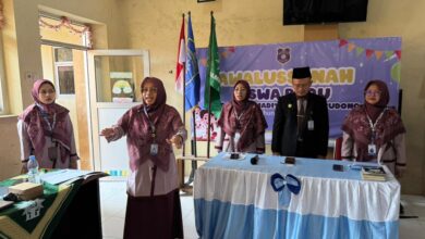 Empat orang pengurus sekolah atau guru sedang berdiri di depan peserta dalam acara formal sekolah, dengan latar belakang spanduk bertuliskan "SD Muhammadiyah".