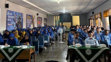 Peserta seminar yang terdiri dari bapak-bapak dan ibu-ibu dengan seragam biru sedang duduk rapi menyimak acara di dalam ruangan aula.