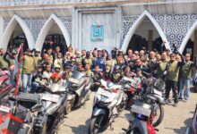Sekelompok anggota komunitas motor dengan rompi seragam berfoto bersama di depan Masjid Al-Aqom dengan sepeda motor mereka.