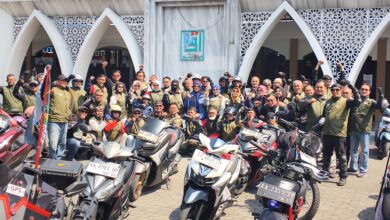 Sekelompok anggota komunitas motor dengan rompi seragam berfoto bersama di depan Masjid Al-Aqom dengan sepeda motor mereka.