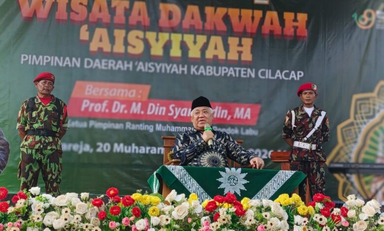 Prof. Dr. M. Din Syamsuddin, MA, memberikan sambutan di panggung Wisata Dakwah Aisyiyah PDA Cilacap, didampingi dua anggota KOKAM. Di depan panggung terdapat rangkaian bunga yang indah.