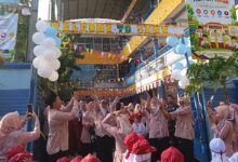 Suasana meriah pembukaan MPLS SD Muhammadiyah Kriyan 2026. Para guru dan orang tua bersorak melempar kertas konfeti ke udara di bawah spanduk besar 'Sekolah Ramah Anak' dan 'International Class Program (ICP)' serta balon putih biru di gerbang sekolah, disaksikan oleh murid baru bertopi merah.