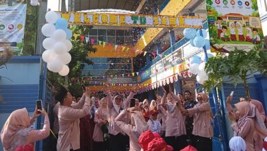 Suasana meriah pembukaan MPLS SD Muhammadiyah Kriyan 2026. Para guru dan orang tua bersorak melempar kertas konfeti ke udara di bawah spanduk besar 'Sekolah Ramah Anak' dan 'International Class Program (ICP)' serta balon putih biru di gerbang sekolah, disaksikan oleh murid baru bertopi merah.