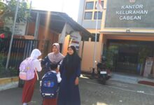 Dua orang guru menyambut siswa SD Muhammadiyah Semarang yang membawa tas ransel di halaman depan Kantor Kelurahan Cabean Semarang Barat.