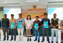 Sembilan orang pria berdiri berpose di depan spanduk pelatihan di sebuah ruangan.