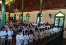Ratusan siswa SD Muhammadiyah 1 Solo berseragam putih dan mukena berbaris rapih khusyuk menunaikan salat berjamaah di dalam masjid dengan pilar kayu hijau.