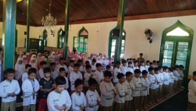 Ratusan siswa SD Muhammadiyah 1 Solo berseragam putih dan mukena berbaris rapih khusyuk menunaikan salat berjamaah di dalam masjid dengan pilar kayu hijau.
