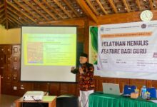 Seorang pemateri sedang menjelaskan teknik menulis feature di depan proyektor saat pelatihan bagi guru.