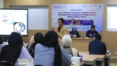Sriyanto sedang memberikan materi seminar di depan peserta, fokus pada cara menulis artikel ilmiah standar ScienceDirect, dengan spanduk seminar "From Research to Impact: Menulis Jurnal Bereputasi dan Mengukur Pengaruh Riset melalui Bibliometrika" di latar belakang.