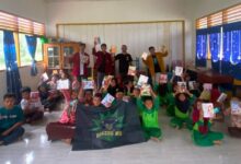 Sekelompok anak sekolah dasar berseragam hijau di dalam kelas sedang berpose bersama anggota BikersMu, menunjukkan buku-buku baru yang mereka terima sebagai bagian dari aksi sosial. Di bagian depan tengah, terdapat bendera atau spanduk hitam bertuliskan "BIKERS MU".