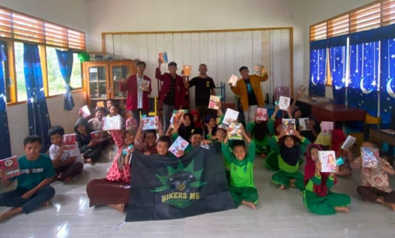 Sekelompok anak sekolah dasar berseragam hijau di dalam kelas sedang berpose bersama anggota BikersMu, menunjukkan buku-buku baru yang mereka terima sebagai bagian dari aksi sosial. Di bagian depan tengah, terdapat bendera atau spanduk hitam bertuliskan "BIKERS MU".