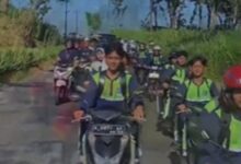 Sejumlah siswa berseragam sekolah dan rompi keselamatan berkendara sepeda motor secara beriringan di jalan pedesaan yang dikelilingi pepohonan.