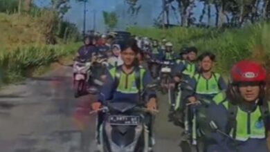 Sejumlah siswa berseragam sekolah dan rompi keselamatan berkendara sepeda motor secara beriringan di jalan pedesaan yang dikelilingi pepohonan.