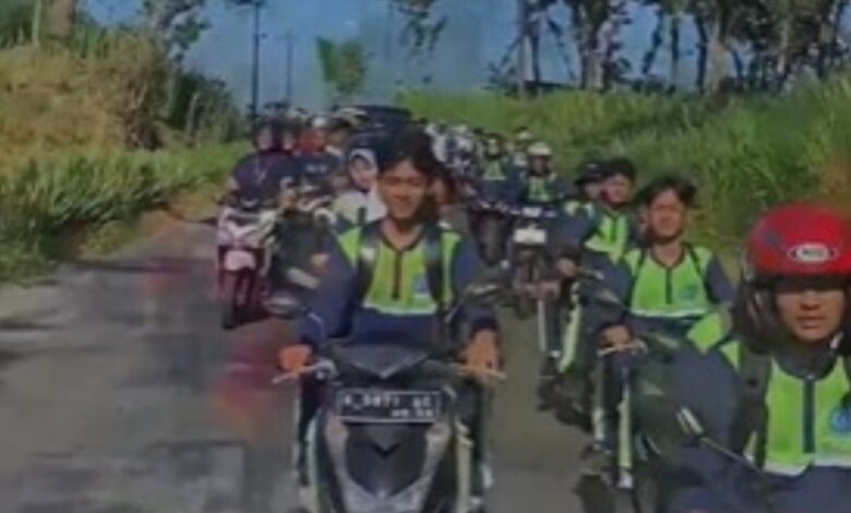 Sejumlah siswa berseragam sekolah dan rompi keselamatan berkendara sepeda motor secara beriringan di jalan pedesaan yang dikelilingi pepohonan.