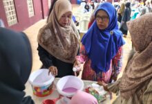 Seorang instruktur perempuan berjilbab biru memberikan demonstrasi praktis pembuatan softener kepada peserta pelatihan wirausaha.