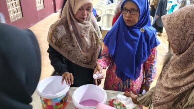 Seorang instruktur perempuan berjilbab biru memberikan demonstrasi praktis pembuatan softener kepada peserta pelatihan wirausaha.