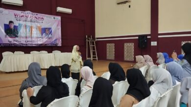 Seorang narasumber sedang memberikan materi pelatihan wirausaha pembuatan softener kepada audiens perempuan di dalam aula pertemuan.