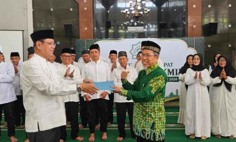 Seorang pria memberikan dokumen kepada pria lain dalam prosesi pelantikan resmi di depan jajaran pengurus organisasi dengan latar belakang spanduk acara.
