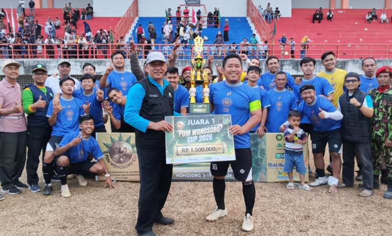 Tim sepak bola berpose bersama membawa piala dan papan simbolis Juara 1 PDM Wonosobo Cup 2026 di lapangan stadion setelah pertandingan final.