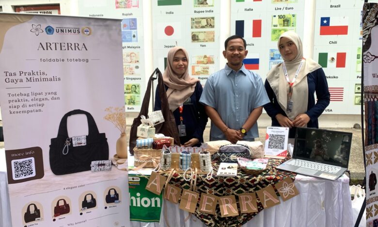 Tim mahasiswa berpose di stan pameran produk tas lipat "Arterra" dengan spanduk promosi dan berbagai contoh produk di meja.