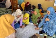 Sekelompok ibu rumah tangga berhijab sedang berdiskusi kelompok (FGD) dan menulis di kertas plano besar dalam acara pelatihan kesehatan mental di Wonogiri.