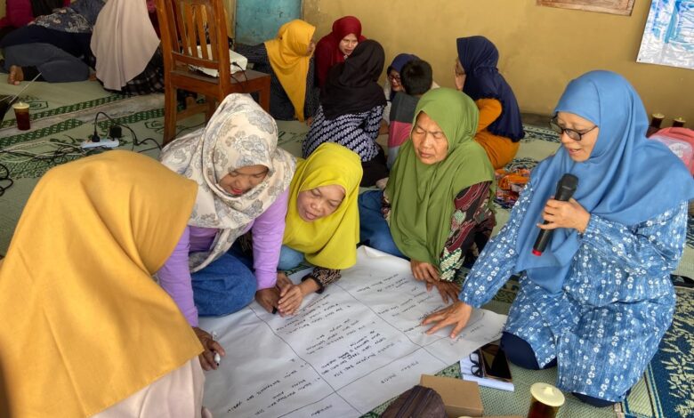 Sekelompok ibu rumah tangga berhijab sedang berdiskusi kelompok (FGD) dan menulis di kertas plano besar dalam acara pelatihan kesehatan mental di Wonogiri.