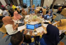 Suasana para peserta lokakarya sedang berdiskusi di meja bundar menggunakan laptop dalam acara pelatihan.