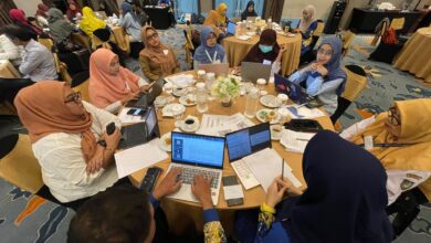 Suasana para peserta lokakarya sedang berdiskusi di meja bundar menggunakan laptop dalam acara pelatihan.