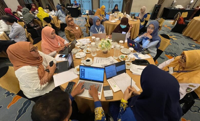 Suasana para peserta lokakarya sedang berdiskusi di meja bundar menggunakan laptop dalam acara pelatihan.