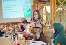 Wakil Direktur II AKMT Min Adadiyah memberikan sambutan dalam acara kolaborasi dengan Penata Anestesi (IPAI) di Temanggung. Di latar belakang terlihat layar proyektor menampilkan logo AKMT dan judul Program Studi D4 Keperawatan Anestesiologi.