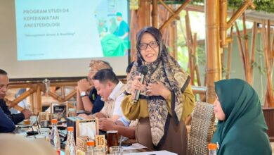 Wakil Direktur II AKMT Min Adadiyah memberikan sambutan dalam acara kolaborasi dengan Penata Anestesi (IPAI) di Temanggung. Di latar belakang terlihat layar proyektor menampilkan logo AKMT dan judul Program Studi D4 Keperawatan Anestesiologi.