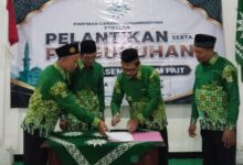 Prosesi penandatanganan berkas pelantikan pengurus Pimpinan Cabang Muhammadiyah (PCM) Siwalan yang disaksikan oleh para pengurus mengenakan seragam hijau batik khas Muhammadiyah.