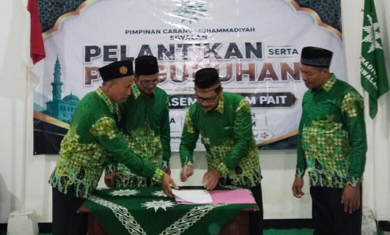 Prosesi penandatanganan berkas pelantikan pengurus Pimpinan Cabang Muhammadiyah (PCM) Siwalan yang disaksikan oleh para pengurus mengenakan seragam hijau batik khas Muhammadiyah.