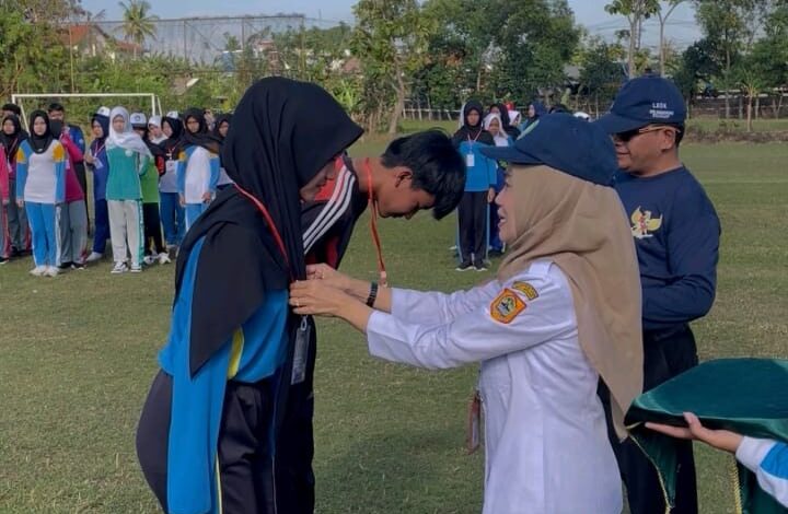 Seorang pejabat wanita sedang menyematkan tanda pengenal kepada peserta pelatihan disiplin di tengah lapangan.