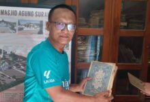 Seorang pria berkacamata mengenakan kaos hijau menunjukkan kitab Al-Qur'an kuno di kompleks Masjid Agung Surakarta.