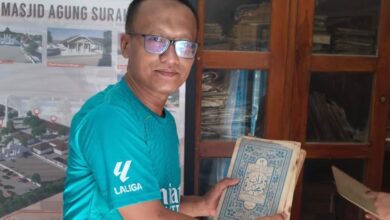 Seorang pria berkacamata mengenakan kaos hijau menunjukkan kitab Al-Qur'an kuno di kompleks Masjid Agung Surakarta.