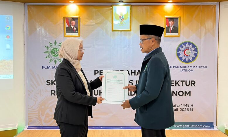 Seorang wanita mengenakan jas hitam dan jilbab menyerahkan dokumen SK resmi kepada seorang pria berjas dan berkopiah hitam di acara PCM Jatinom.
