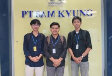 Tiga orang pria mengenakan kemeja dan ID card berpose bersama di depan logo dan papan nama PT Sam Kyung.