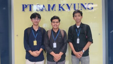 Tiga orang pria mengenakan kemeja dan ID card berpose bersama di depan logo dan papan nama PT Sam Kyung.