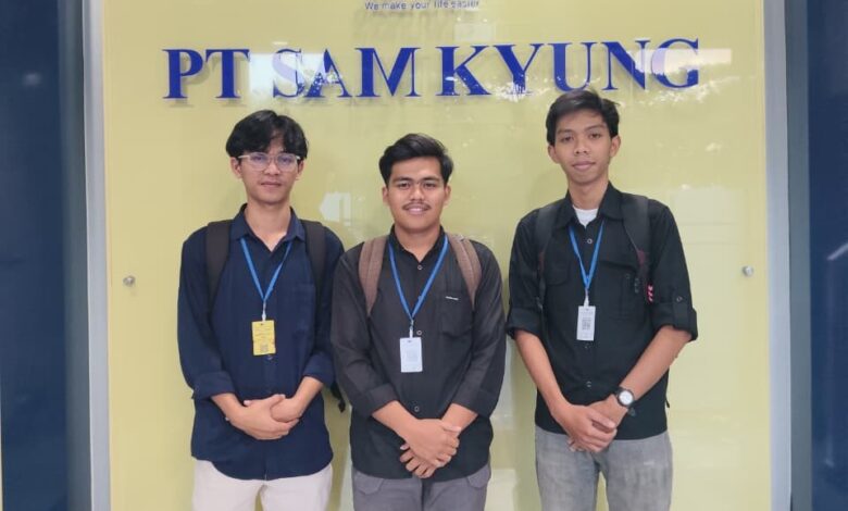 Tiga orang pria mengenakan kemeja dan ID card berpose bersama di depan logo dan papan nama PT Sam Kyung.