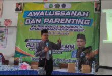 Seorang narasumber berdiri menyampaikan materi di depan banner acara Awalussanah dan Parenting RA Perwanida Munggur serta MI Muhammadiyah Munggur.