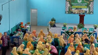 Sekelompok wanita berpakaian kuning dan jilbab senada sedang duduk berkelompok di sekitar meja hijau di dalam ruangan aula yang luas, sedang mengikuti kegiatan pelatihan mitigasi bencana banjir. Di depan, seorang pria berbaju batik memberikan presentasi. Ada spanduk hijau di dinding dengan tulisan "Pertemuan Periodik Ranting se-Kecamatan Tambak". Spanduk tersebut menunjukkan partisipasi 'Aisyiyah dalam kegiatan tersebut. Pemandangan dari atas.