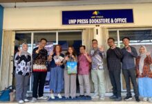 Rombongan tamu berpose bersama sambil menunjukkan gestur tangan di depan papan nama UMP Press Bookstore & Office.