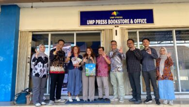 Rombongan tamu berpose bersama sambil menunjukkan gestur tangan di depan papan nama UMP Press Bookstore & Office.