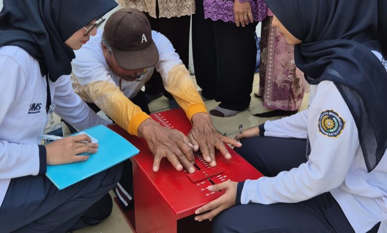 Dua mahasiswi berhijab dari UMS membantu seorang pria paruh baya melakukan tes fleksibilitas menggunakan alat ukur sit and reach berwarna merah.