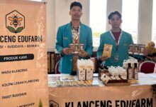 Dua mahasiswa mengenakan jas almamater biru berdiri di stan pameran Klanceng Edufarm sambil memamerkan produk madu dan brosur.