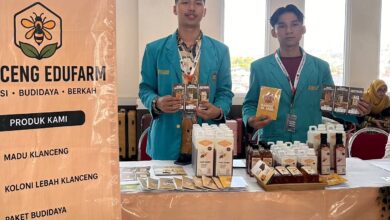 Dua mahasiswa mengenakan jas almamater biru berdiri di stan pameran Klanceng Edufarm sambil memamerkan produk madu dan brosur.