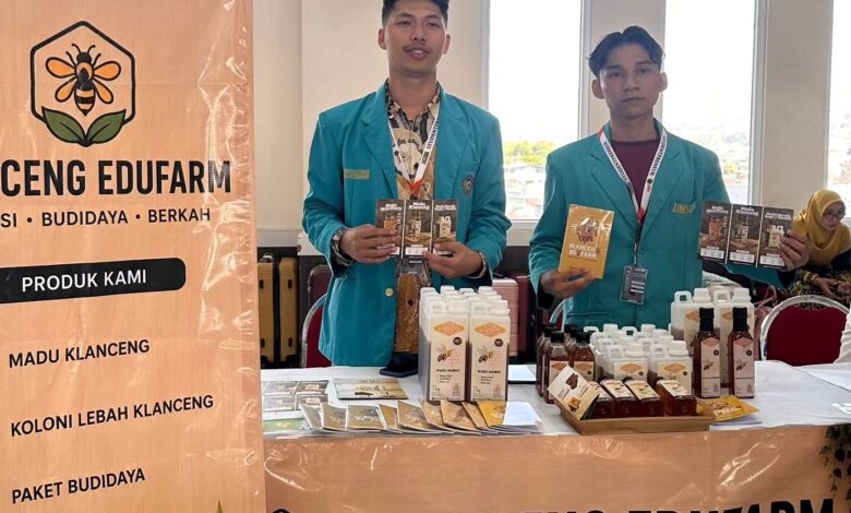 Dua mahasiswa mengenakan jas almamater biru berdiri di stan pameran Klanceng Edufarm sambil memamerkan produk madu dan brosur.