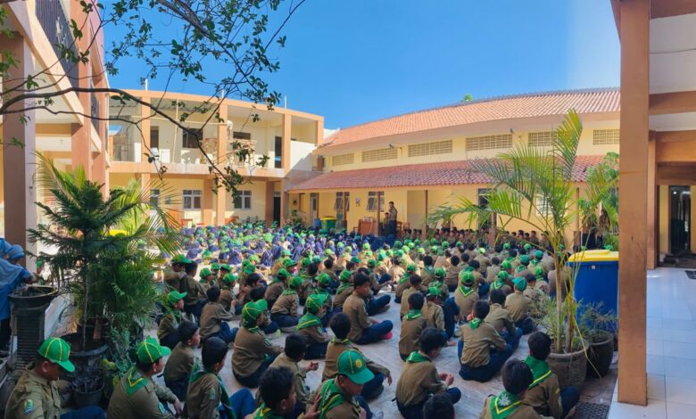 Ratusan siswa berseragam pramuka duduk rapi di halaman sekolah mendengarkan pengarahan.